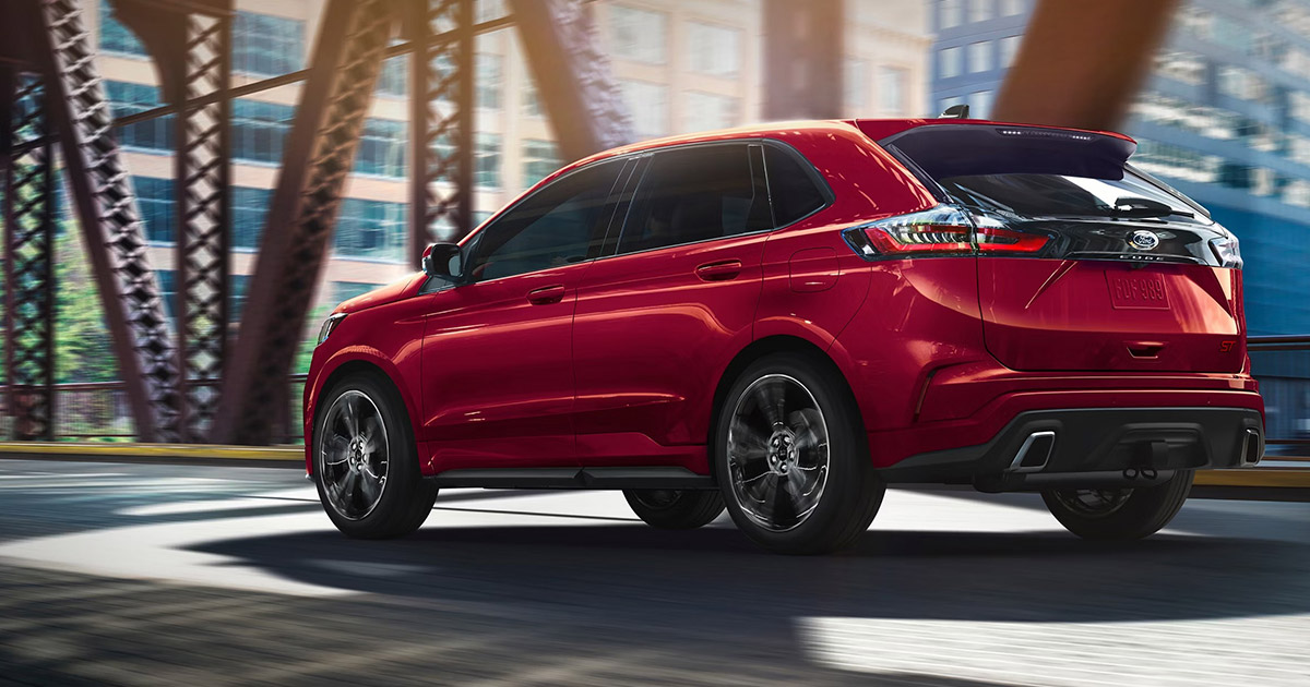 Red Ford Edge ST SUV driving dynamically on urban street with modern buildings and steel structures in background
