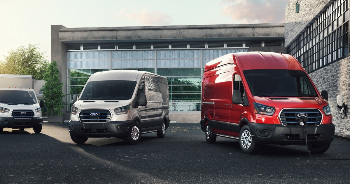 Three Ford Transit vans in white and red, parked near a modern building with glass and stone facade