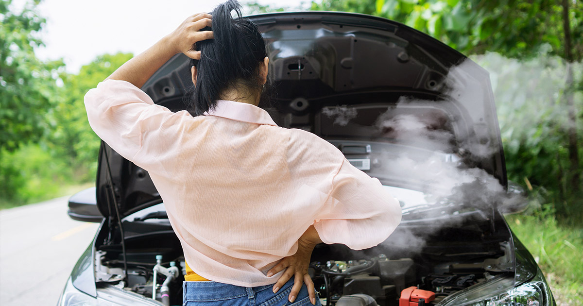 Stressed driver looking at steaming car engine on roadside, potential vehicle breakdown situation