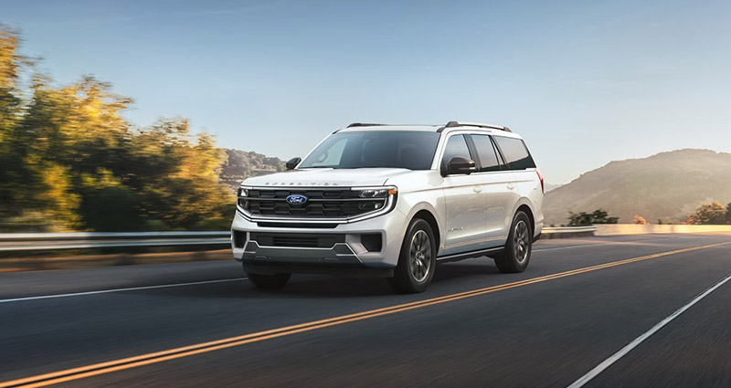 White 2024 Ford Expedition SUV driving on mountain highway with scenic background, powerful and sleek design