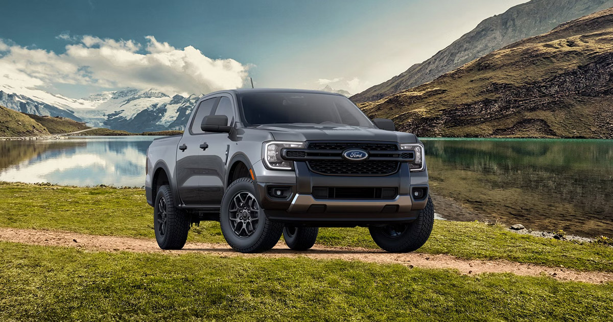 Grey 2024 Ford Ranger pickup truck parked on grassy lakeside trail with snow-capped mountains in background