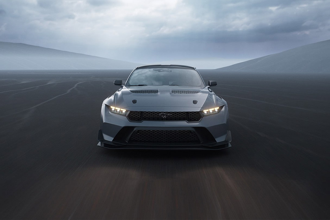 Ford Mustang GT performance car with LED headlights, silver color, on misty road with mountains background