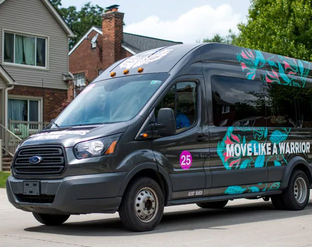 Black Ford Transit passenger van with "Move Like a Warrior" graphic design, parked on residential street
