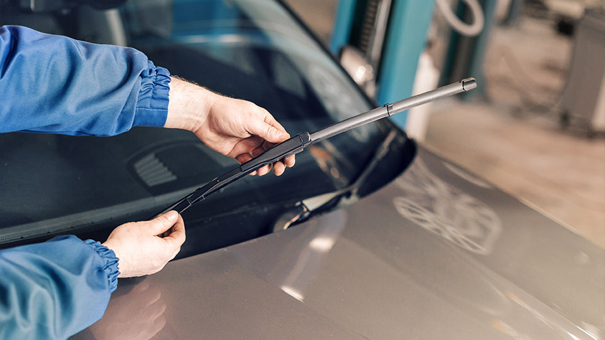 Auto technician replacing windshield wiper blade on Ford vehicle during routine maintenance service