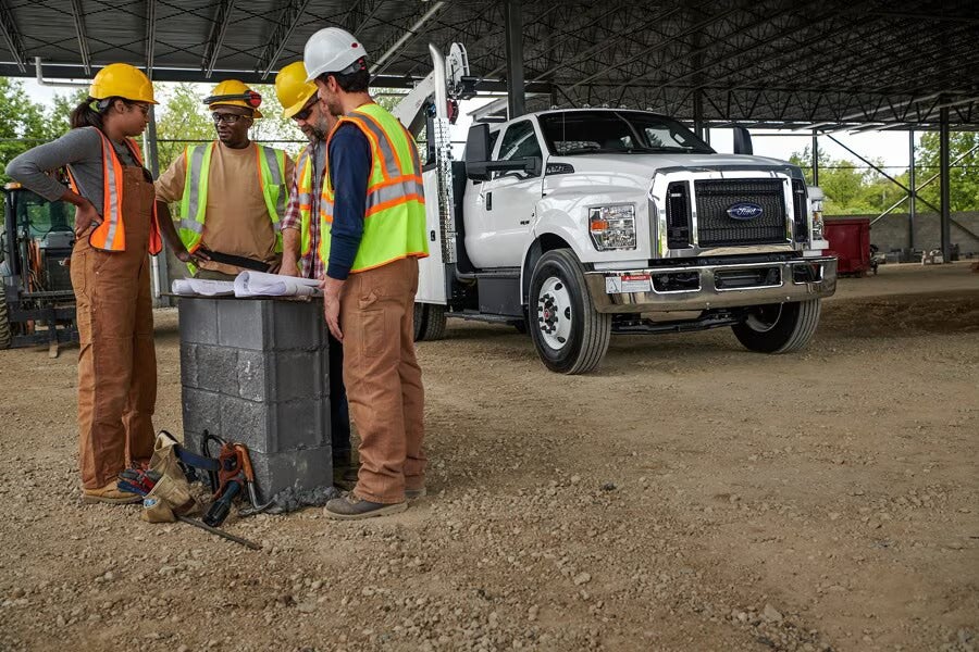 Construction workers reviewing blueprints near a white Ford truck